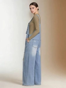 Detail of light blue distressed denim overalls with vintage ripped texture and side buckles