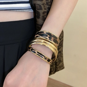 Detail of leopard print leather texture and polished gold metal bangles on model wrist