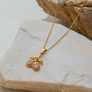Golden cherry pendant necklace with pink zircons displayed on a natural stone surface