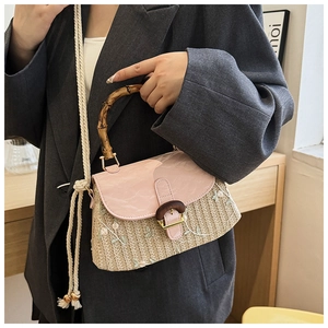 Detail of floral embroidery and bamboo handle on the woven straw crossbody bag
