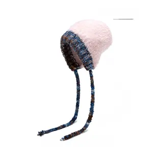 Détail d'un bonnet en maille rose avec de longues lanières tressées bleues et marron