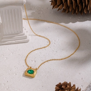Close-up of gold square pendant necklace with oval green gemstone on white stone base