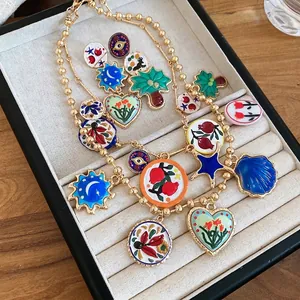 Golden bead chain necklace set with colorful enamel heart and sun pendants on a beige tray