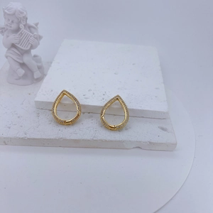 Close-up of golden teardrop earrings with pavé zircons on decorative plaster layers
