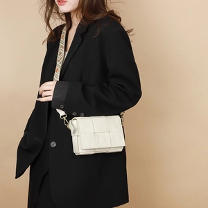 Close-up of white woven leather crossbody bag featuring a stylish geometric pattern wide strap