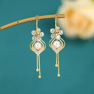 Macro detail of long gold tassel earrings with zircon flower and pearl element