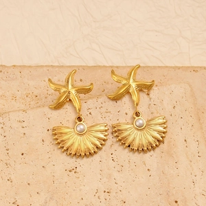 Gold starfish earrings with shell charms and pearls over a neutral textured stone background