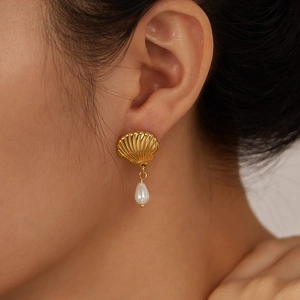 Close-up of a model wearing a gold shell earring featuring a white drop pearl pendant