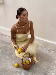 Detail of light yellow knitted maxi dress texture with elegant gold necklace and accessories