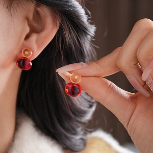 Detail of red and amber resin double sphere stud earrings worn by a model in soft light