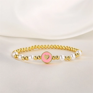 Détail d'un bracelet perlé avec billes dorées, perles blanches et breloque cœur rose