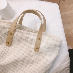 Detail of woven fabric texture and brown leather handles with brass rivets on tote bag