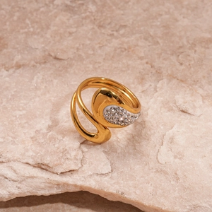 Macro detail of a gold-plated wavy ring with crystal pavé on a textured stone surface