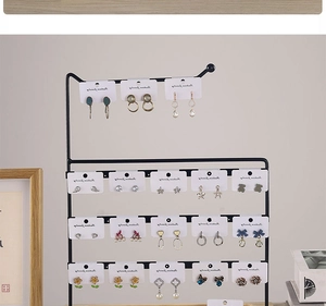 Black iron earring stand with white cards displaying jewelry on a desktop