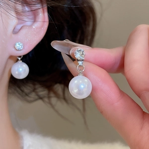 Close-up of elegant pearl drop earring with sparkling zircon stud on silver needle