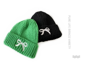 Close-up of knitted beanies in green and black with white bow embroidery details