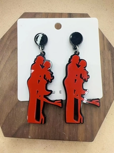 Detail of red and black acrylic earrings featuring a romantic silhouette on a wood surface