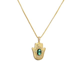 Detail of golden Hamsa Hand pendant with green oval gemstone and clear accents