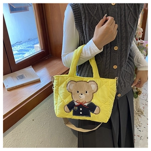 Girl carrying a yellow quilted teddy bear tote bag with shoulder strap in a cozy room