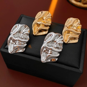 Macro shot of gold and silver irregular crinkled metal stud earrings on black leather