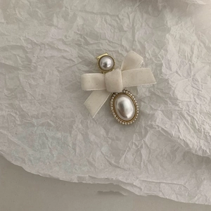 Detail of a creamy white velvet bow hair clip with a gold-rimmed pearl accent