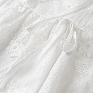 Detail shot of white fabric featuring intricate floral embroidery and a delicate drawstring bow