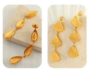 Macro detail of golden water-drop and shell-shaped dangling earrings on white fabric