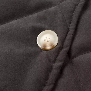 Close-up of a high-quality light-colored four-hole button on quilted diamond cotton jacket