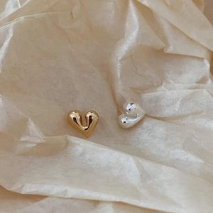 Detailed close-up of gold and silver minimalist heart earrings on beige textured background