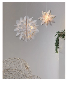 Close-up of a white paper snowflake lantern with warm LED light against a grey wall