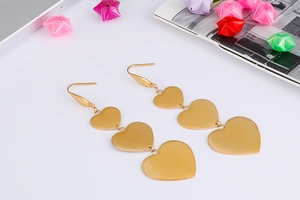Detailed view of triple gold heart drop earrings with matte finish on white background