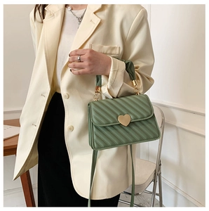 Close-up of avocado green quilted handbag with a heart-shaped gold metal lock and handle