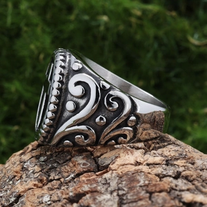 Vintage stainless steel cross ring with intricate floral carvings on rustic bark base