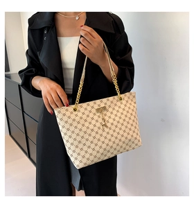 Detail of cream tote bag with cross pattern, gold chain strap and deer pendant accessory