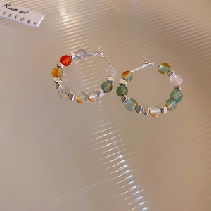 Macro shot of silver geometric hoop earrings with colorful beads on textured background