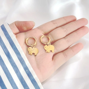 Macro shot of gold elephant earrings on hand with soft white silk background