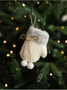 Close-up of a white knitted Christmas glove ornament with wood button on a pine tree