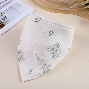 Flat lay of a beige muslin baby bib with green floral patterns on a wooden tray