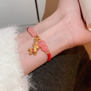 Détail macro du bracelet en fil rouge tressé avec perles roses et breloque cheval doré