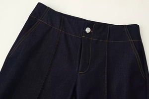 Gros plan d'un jean bleu indigo avec coutures orange contrastées et bouton en métal argenté
