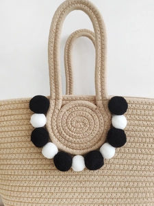 Handmade woven straw tote bag with decorative black and white pom-poms for beach travel