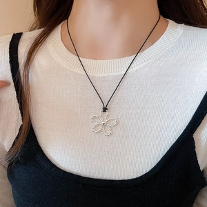 Détail du pendentif fleur argentée sur cordon noir porté sur un tricot blanc