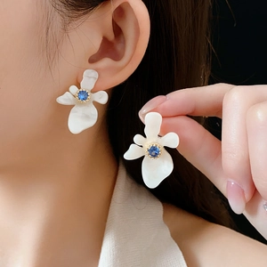 Gros plan sur des boucles d'oreilles fleurs en résine blanche et zircons bleus avec billes d'or