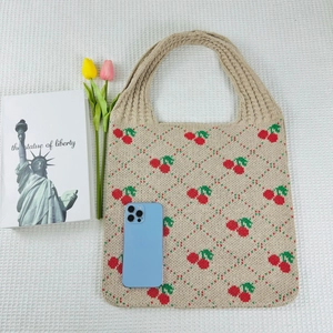 Beige knit tote bag with cherry patterns shown with lifestyle props on white fabric