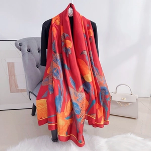 Red silk scarf featuring blue and orange floral prints draped over a grey modern chair