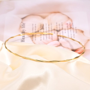 Detail of minimalist 18K gold twisted collar necklace on a soft silk background