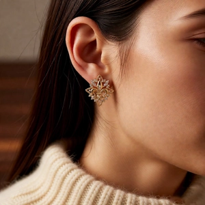 Close-up of a gold 18k plated fleur-de-lis stud earring with zircons on model ear