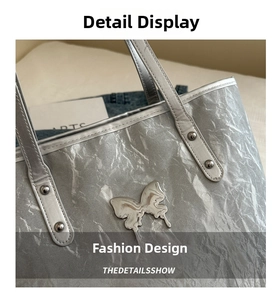 Detail of silver metallic tote bag featuring liquid metal butterfly badge and crinkled texture