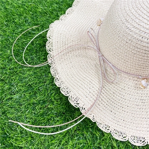 Détail du chapeau de soleil en paille avec bord ondulé et nœud avec pendentifs