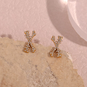 Detailed close-up of golden X-shaped stud earrings featuring sparkling white crystals